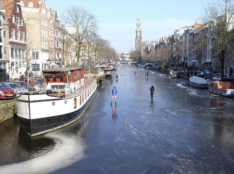 People walk and skate on the frozen Prinsengracht canal in downtown Amsterdam, Friday, March 2, 2018. The icy weather gripping much of Europe is good news for the Dutch, many of whom love to skate on frozen waterways if the weather allows. (AP Photo/Mike Corder)
