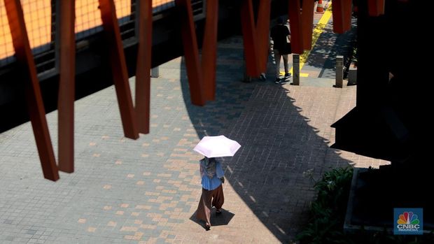 Pejalan kaki menggunakan payung untuk menghindari terik matahari di kawasan Jembatan Pinisi di halte busway Karet, Jakarta, Rabu (27/9/2023). (CNBC Indonesia/Muhammad Sabki)