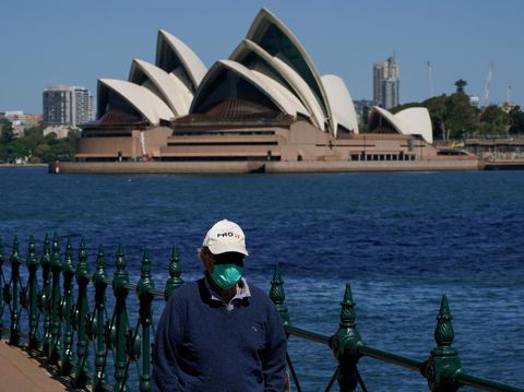 FILE PHOTO: A person in protective face mask walks along the harbour waterfront across from the Sydney Opera House during a lockdown to curb the spread of coronavirus disease (COVID-19) outbreak in Sydney, Australia, October 6, 2021. REUTERS/Loren Elliott/File Photo