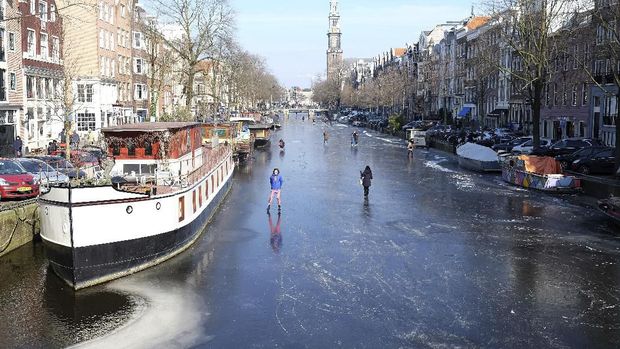 People walk and skate on the frozen Prinsengracht canal in downtown Amsterdam, Friday, March 2, 2018. The icy weather gripping much of Europe is good news for the Dutch, many of whom love to skate on frozen waterways if the weather allows. (AP Photo/Mike Corder)