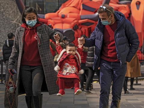 A couple wearing face masks to help curb the spread of the coronavirus lift their child wearing a new year costume as they visit to the capital city's popular shopping mall during the first day of the Lunar New Year in Beijing, Friday, Feb. 12, 2021. Festivities for the holiday, normally East Asia's busiest tourism season, are muted after China, Vietnam, Taiwan and other governments tightened travel curbs and urged the public to avoid big gatherings following renewed virus outbreaks. (AP Photo/Andy Wong)